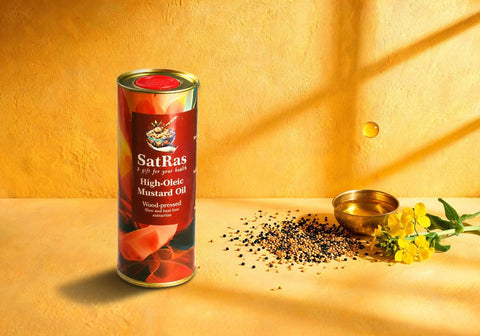 SatRas wood-pressed high oleic mustard oil tin on a saffron backdrop beside black and yellow mustard seeds and a brass bowl of oil